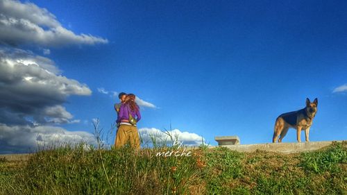 Woman standing on grass against blue sky