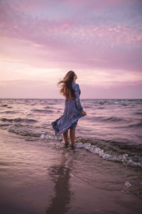 Woman standing on shore at beach during sunset