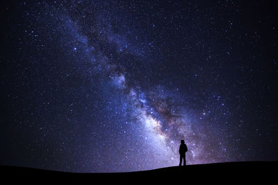 Low angle view of silhouette person standing on field against star field