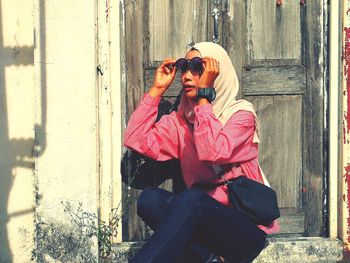 Young woman wearing sunglasses while sitting against doors