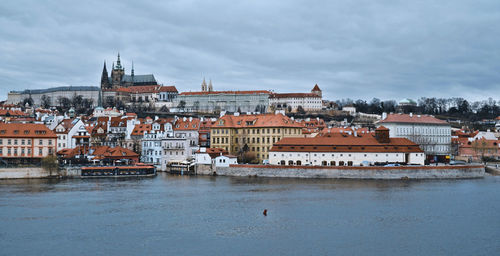 Buildings at waterfront against cloudy sky