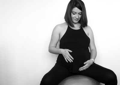 Smiling pregnant woman sitting on fitness ball against white background