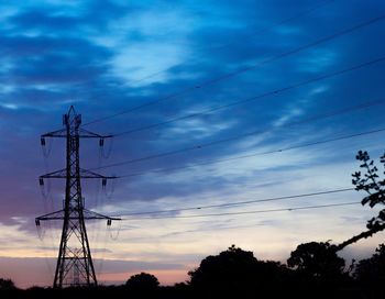 Low angle view of electricity pylon against cloudy sky