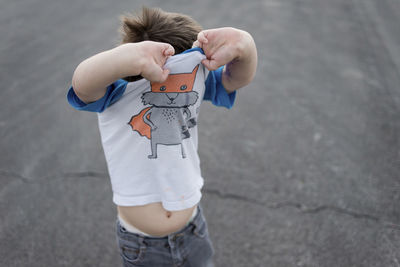 High angle view of boy removing t-shirt while standing on footpath