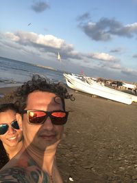 Portrait of young man on sunglasses at beach against sky