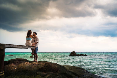 Friends on rock by sea against sky