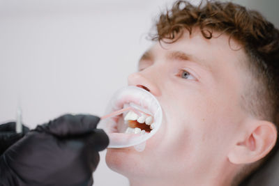 Close-up of young woman holding dentures against white background