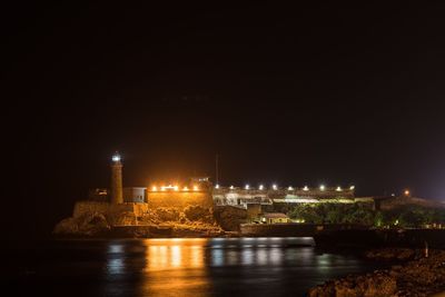 Illuminated buildings by river against sky at night