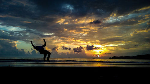 Silhouette man on beach against sky during sunset