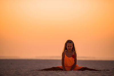 Smiling girl sitting on beach against clear sky during sunset