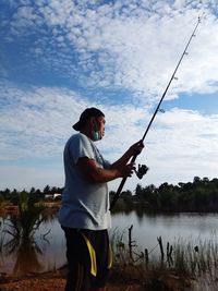 Side view of man fishing in lake against sky