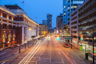 Light trails on street amidst buildings in city against sky at night