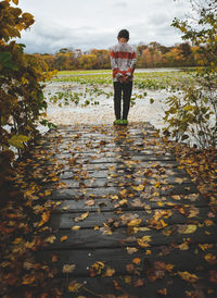 Full length rear view of boy standing by lake during autumn