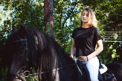 Young woman riding with horse against trees
