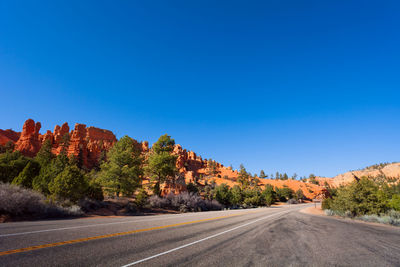 Road by trees against clear blue sky