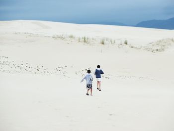 Rear view of boys walking on sand at desert