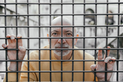 Older man with a gentle smile viewed through black metal bars, enhancing his expressive eyes