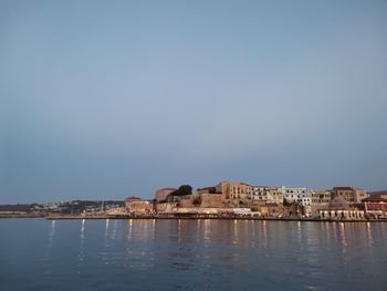 Sea by buildings against clear sky