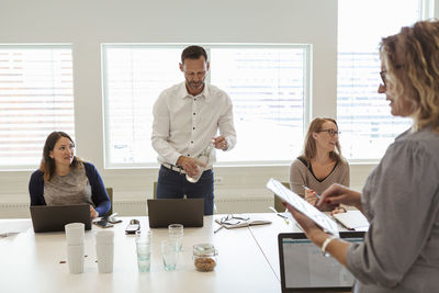 Businessman drinking water while colleagues discussing in meeting at office