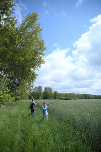Boys walking with fishing rods on grassy field against sky