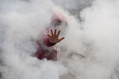 Man in hood standing amidst smoke