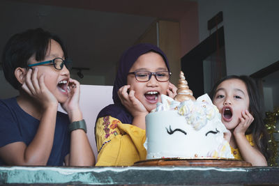 Low angle view of cheerful siblings screaming while looking at birthday cake