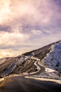 Road by mountains against cloudy sky in winter during sunset