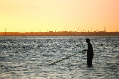 Silhouette fisherman standing with fishing net in sea against sky during sunset