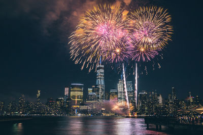 Low angle view of firework display over river in city at night