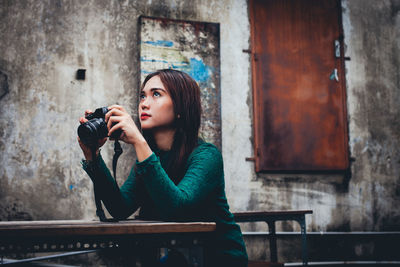 Portrait of young woman looking away while sitting on wall