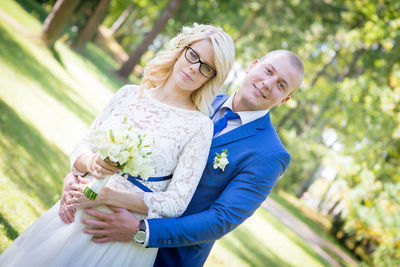 Portrait of bride and bridegroom standing against trees at park
