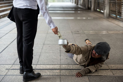 Low section of businessman putting paper currency in bowl held by beggar