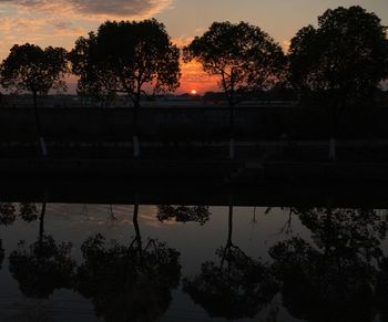 Silhouette trees by lake against sky during sunset