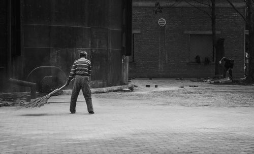 Full length rear view of sweeper cleaning street against building