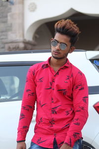 Young man wearing sunglasses standing by car