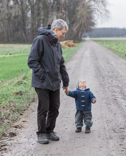 Full length of mature man standing with granddaughter on dirt road