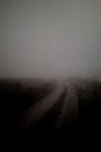 Dirt road on field against sky during foggy weather