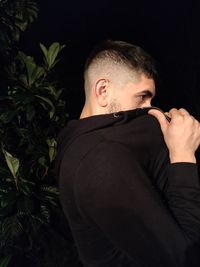 Young man looking away while standing against black background