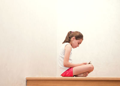 Side view of girl sitting against wall at home