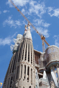 Low angle view of crane by building against sky