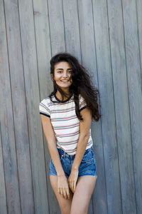 Portrait of young woman standing against wooden wall