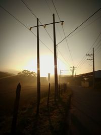 Electricity pylon on landscape against sky during sunset