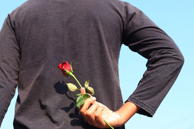 Close-up of man holding red flower against white background