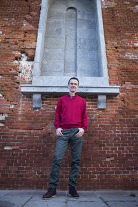 Portrait of young man standing against brick wall