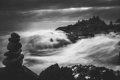 Stack of stones on rocky shore against cloudy sky