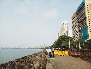 Rear view of people on sea by buildings against sky