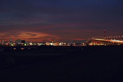 Illuminated buildings by road against sky at night