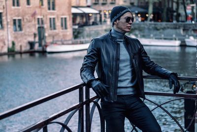 Man looking away while leaning on railing against river in city