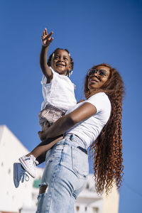 Young woman carrying daughter under blue sky