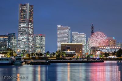 Illuminated city by river against sky at night
